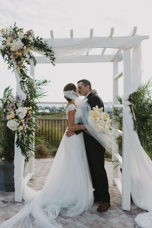 a man and woman kissing under a white arbor
